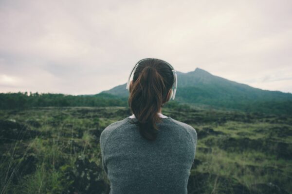Female with brown hair tied up, wearing headphones looking towards a large grassy hill