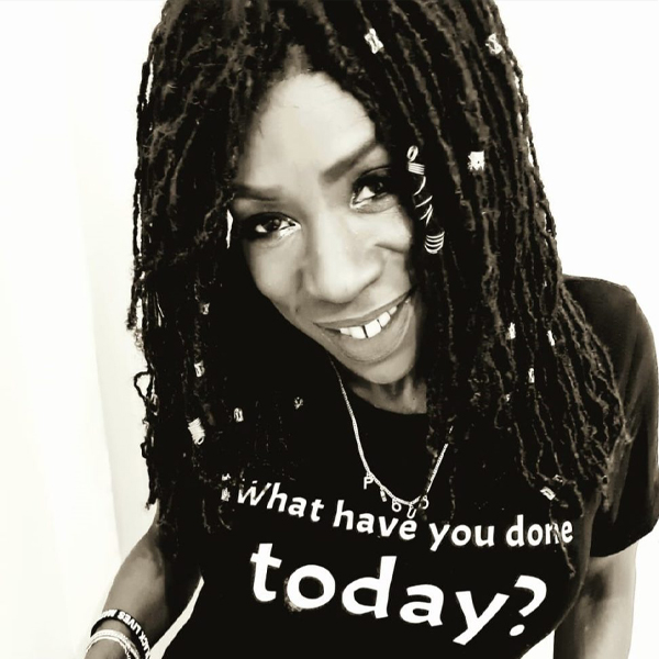 Heather Small in black and white, wearing a T-Shirt with the text What have you done today? on it, she has her hair braided in a protective style with silver charms woven in