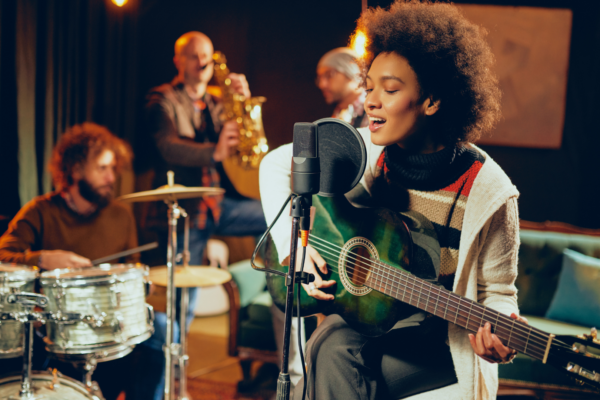 A band plays in the background with a singer singing into a microphone while playing an acoustic guitar