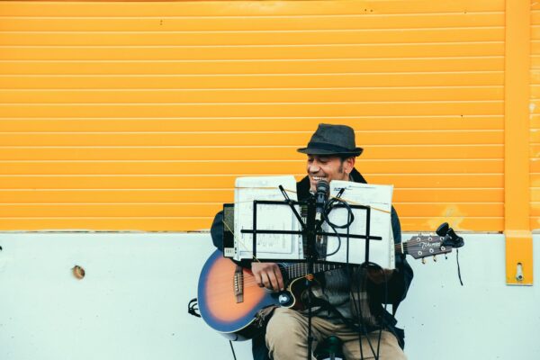 A man busking playing a guitar and singing sheet music, he is playing in front of yellow shutters