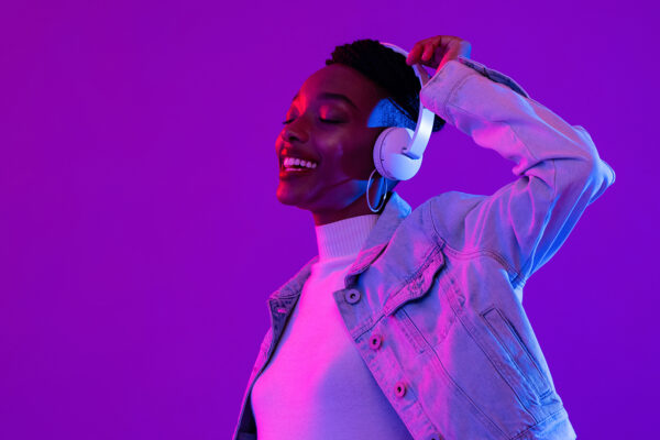 Black woman wearing headphones listening to music and dancing on a purple background