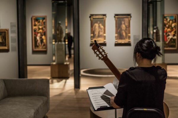 A person turned away from the camera, playing a guitar to an art gallery room