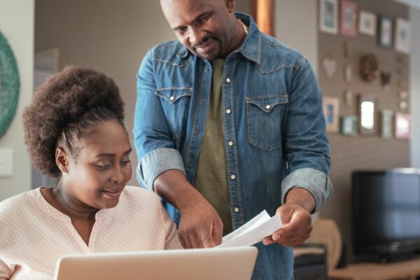 A couple looking at a piece of paper, the man is wearing a blue denim shirt, the woman has tight curly black hair and is wearing a pink blouse