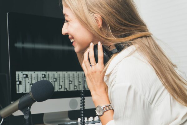A blonde woman smiling into a microphone in a recording studio