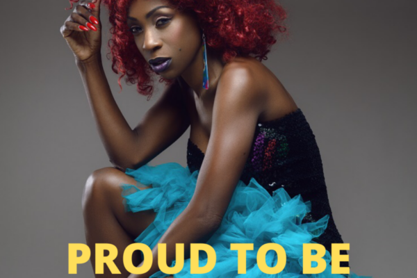 Heather Small with red curly hair, a glittery dress and blue tutu, she is wearing black lipstick and has large earrings and red nails, the text below reads Proud To Be, Black history month 2021