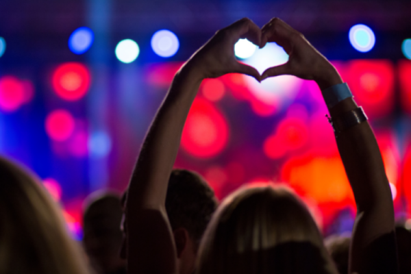 A woman with her hands in the air at a concert making a heart shape with her hands