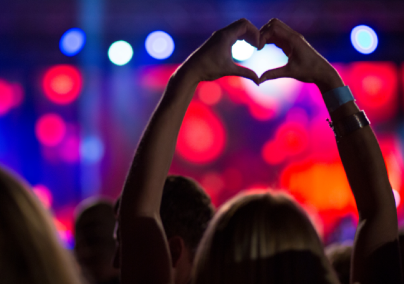 A woman with her hands in the air at a concert making a heart shape with her hands